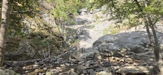 From the trail boardwalk, a view of the falls flowing from the top of the cliff down into a large pool of water.