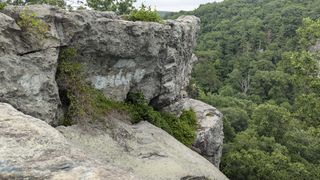 Side profile of the boulders showing more foliage growing. Someone is preparing to rock climb further down the path.